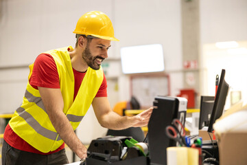 A smiling worker in a hard hat using a computer at a construction site showcasing teamwork and safety.