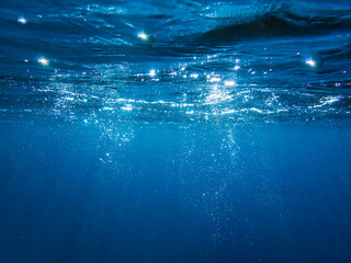 Obraz premium Underwater background with water bubbles and undersea light rays shine. Dark blue ocean surface seen from underwater. Sunbeams and Sea deep or ocean underwater a Abstract background. sunlight Nature.