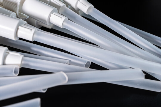 Collection of white plastic dispensing pumps with long tubes arranged on a black surface, showcasing their design and functionality for various container types