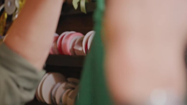 Closeup of florist preparing flowers. Florist finetuning bouquet accessories in cozy workspace environment. Creative floral stylist tweaking ribbon selection and bag strap in warm craft room