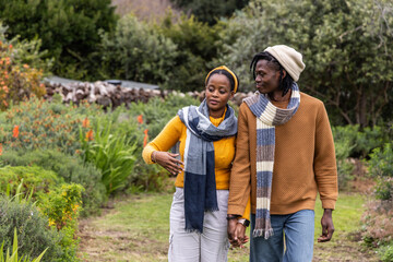 African American couple walking holding hands in garden wearing mustard and rust sweaters, scarves