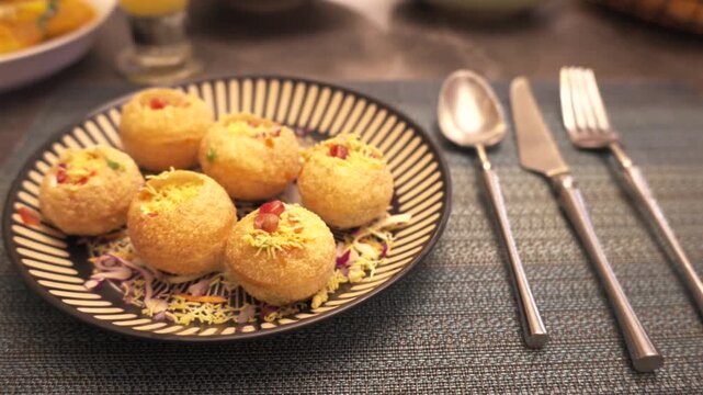 Golden Pani Puri Snacks Served on Patterned Plate with Silver Cutlery in Indian Restaurant Setting,