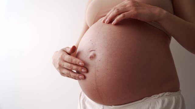 Closeup of impersonal woman, future mother touching naked tummy belly at third trimester showing love, care to baby standing at wall. Pregnant, eco, prenatal maternity, waiting motherhood. Isolated