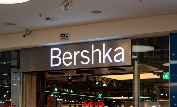 Modern Bershka store signage in a shopping mall, illuminated clothing brand logo above the entrance, youth fashion boutique interior, professional retail spotlight lighting, fitting rooms area, and in