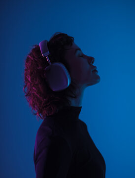 Profile of young woman wearing headphones in blue neon light. Music, focus, technology and modern lifestyle concept.