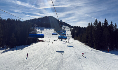 Sunny ski slope with chairlift and skiers in alpine mountains, winter sports resort landscape with blue sky