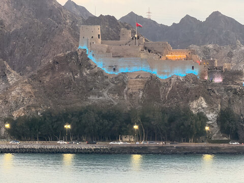 Oman, Muscat - January 08, 2026. Illuminated Muttrah Fort on a rocky hill in Muscat, Oman. Historic castle with blue lights and Omani flag at twilight