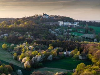 defaultPanorama Góry Świętej Anny o zachodzie słońca. Widok na bazylikę i klasztor na wzgórzu w otoczeniu wiosennej zieleni i kwitnących drzew. Kultowe miejsce kultu i turystyki na Opolszczyźnie. © Henryk Niestrój