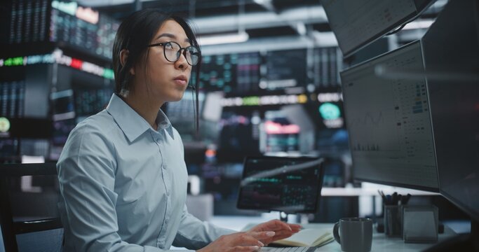Female Trader Executing Stock and Cryptocurrency Deals in Innovative Digital Office. Focused Asian Broker Trading Global Assets Multi Monitor Workstation With Tablet. Professional Market Execution.