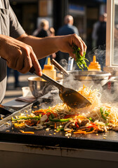 Cooking delicious stir-fry noodles on a hot griddle at an outdoor market.