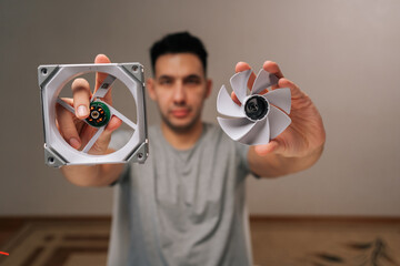 Portrait of technician male holding separated blades and frame of cooling fan, illustrating process...