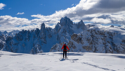 Ski mountaineer crossing a snowy ridge in the Dolomites with dramatic alpine peaks and blue sky in the background, capturing winter adventure and breathtaking mountain landscape.