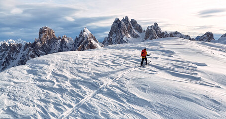 Ski mountaineer crossing a snowy ridge in the Dolomites with dramatic alpine peaks and blue sky in the background, capturing winter adventure and breathtaking mountain landscape.