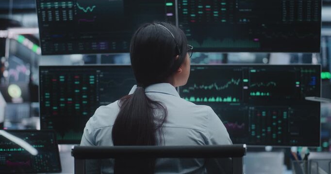 Young Woman Expert Analyzes Market Trends on High Tech Monitors in Massive Digital Office. Concept of Advanced Analytics, Corporate Financial Intelligence and High Speed Electronic Trading Operations.