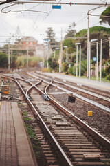 Fototapeta premium Railway tracks merge and split at a quiet station, flanked by soft greenery and distant buildings. The atmosphere feels calm and awaits the sound of arriving trains