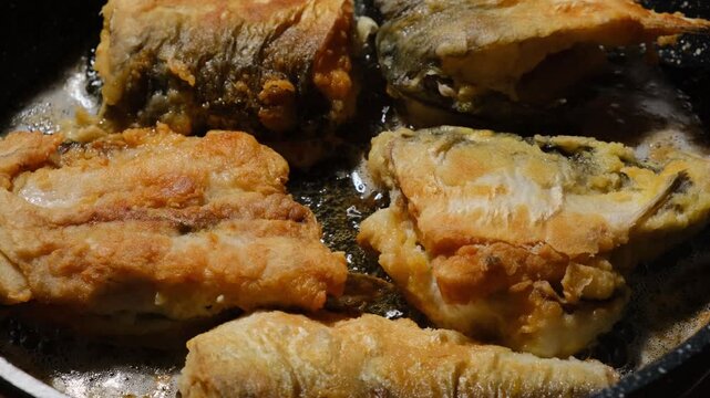Large pieces of fish frying in pan with golden crispy crust. Fish chunks cooking in oil with bubbles. Fish meat rich in iodine and omega fatty acids, thermal processing of seafood.