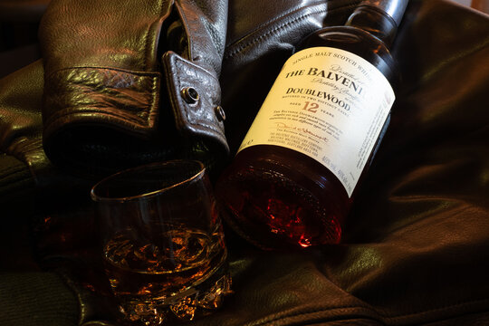 The Balvenie DoubleWood 12 Years Old Scotch whisky and glass spirit on vintage brown leather pilot jacket. Professional lifestyle photography with warm lighting. Ukraine, Zhytomyr, February 26, 2026