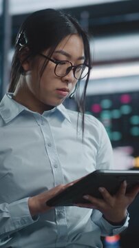 Woman Cross Referencing Real Time Financial Charts on Digital Tablet While Discussing Market Moves in Professional Headset. Concept High Level Multitasking and Expert Data Verification. Vertical Shot.