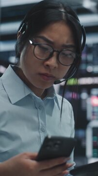 Asian Woman Cross References Real Time Financial Data on Multi Monitor Workstation and Tablet. Female Reports Critical Market Information Contact on Smartphone. Urgent Communication. Vertical Shot.