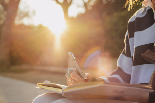 Woman journaling in sunlit park: embracing nature and creativity at golden hour
