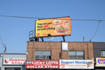 Obraz premium rooftop billboard of McDonald's Canada collab with Frank's Red Hot Sauce and shop signs (Shawarma N' Fries, Lucky Lotto Convenience Dollar Store, Seaport Merchants) Victoria Park Av, Toronto
