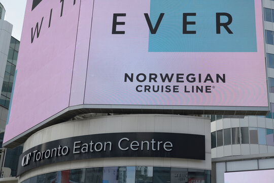 Norwegian Cruise Line advertisement for 2026 on electronic display above entrance to CF Toronto Eaton Centre, facing Sankofa Square, Toronto