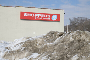 Obraz premium grungy snow pile and wall mounted sign outside Shoppers Drug Mart a pharmacy chain located here at 265 Coxwell Av (seen from Gerrard St E), Toronto
