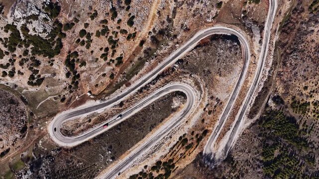 The impressive aerial view of the winding mountain pass. A dynamic drone shot featuring sharp turns and natural rocky terrain.