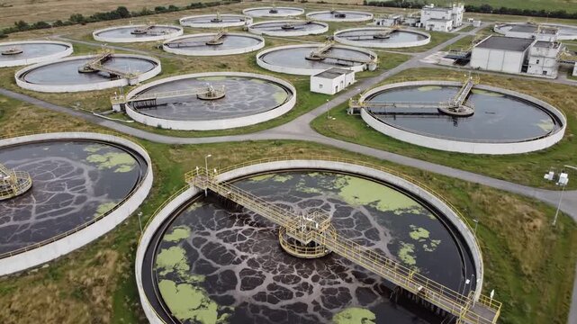 Essential Infrastructure. Aerial view of a large wastewater treatment plant with numerous circular clarifier tanks, perfect for illustrating environmental engineering concepts or urban development.