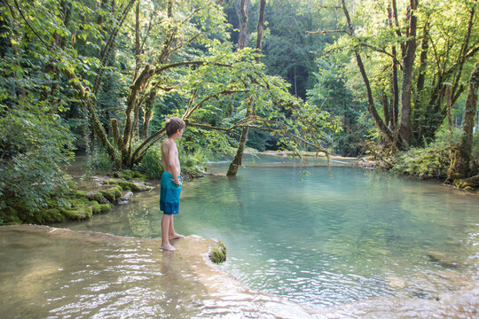 gar&ccedil;on devant cours d'eau du Dard et cascade des tufs en &eacute;t&eacute; dans le Jura pr&egrave;s des Planches-sur-Arbois