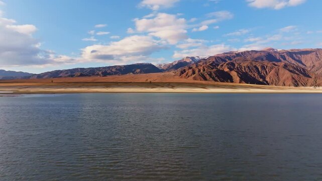 Majestic mountain range towers over a serene Orto Tokoy reservoir in Kyrgyzstan. Clouds drift peacefully above, creating a tranquil outdoor landscape during daytime.