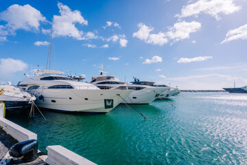 Fototapeta premium Luxury yachts docked at a marina with clear blue waters and a bright sky, showcasing modern boat designs and nautical lifestyle