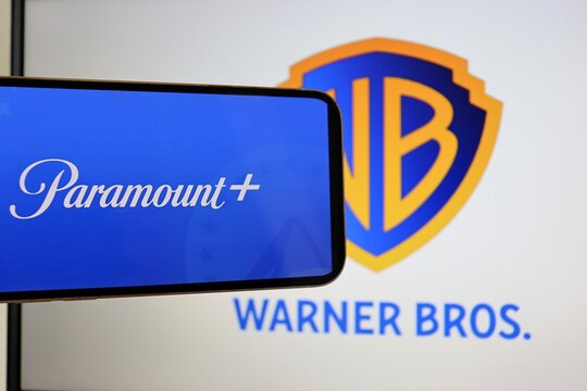 Paramount logo on smartphone screen with Warner Bros logo in the background. Paramount and Warner Bros. 