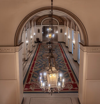 Looking through an archway to a long interior corridor, Chateauesque style  with chandeliers, wall sconces, carpeting, nobody