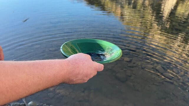 Millennial man (early 40s) wearing a poncho and cowboy hat, panning for gold in Arizona in river