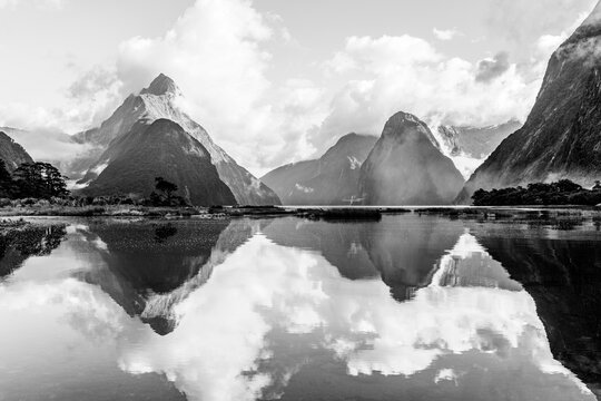 Fiordland National Park, South Island, New Zealand: Majestic landscape of Milford Sound and clouds coverrd Mitre Peak reflected in the water in black and whte