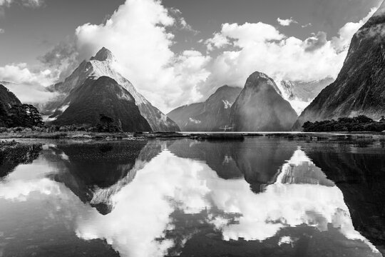 Fiordland National Park, South Island, New Zealand: Majestic landscape of Milford Sound and clouds coverrd Mitre Peak reflected in the water in black and whte