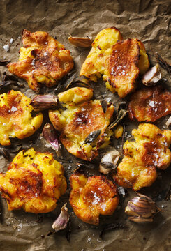 Crispy smashed roast potatoes with garlic and sage sprinkled with salt flakes on gray baking paper, top view