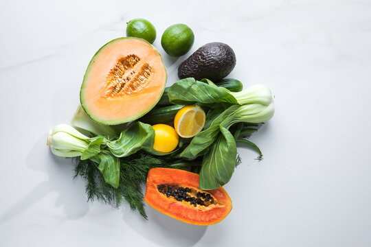 Raw mixed organic vegetables on a white background. Includes avocado, Pac Choi, papaya, melon, lemon