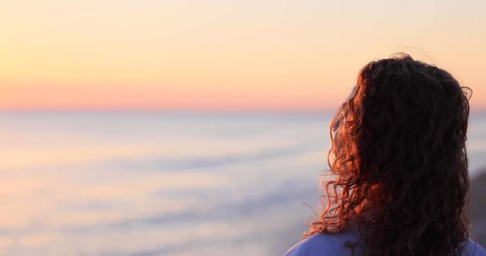 A happy young woman walking at the beach against the sunset during summer vacation. Slow motion