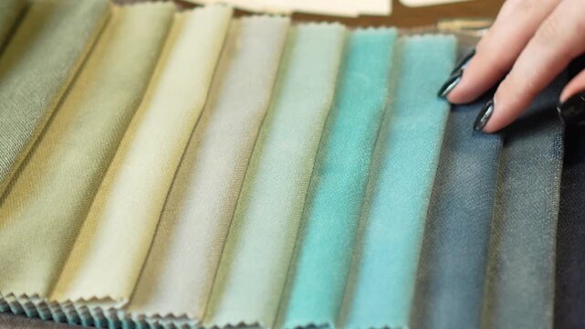 woman touches, irons and chooses blue and green fabric from fabric samples for curtains, textiles and furniture. professional selection of fabric in the salon, interior design, cozy home, tactile