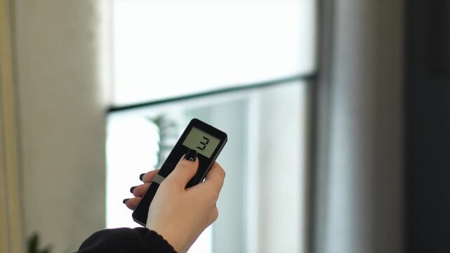 woman controls the remote control for the automatic system of opening and closing the roller blind. professional window shading salon, electric drive, elite technology, curtains on the remote control