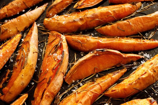 Roasted sliced ​​sweet potatoes with aromatic rosemary and olive oil, sprinkled with salt flakes, close-up view