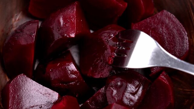 A fork pierces a slice of cooked beetroot in a rustic wooden bowl close up