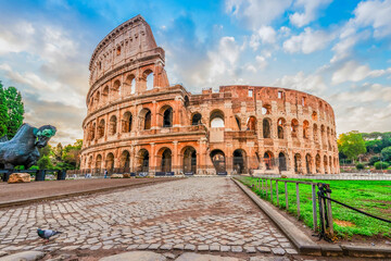 Fototapeta premium ruins of antique Colosseum with green grass lawn in sunise lights, Rome Italy