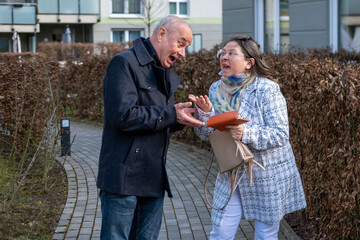 Senior man and adult woman having heated emotional argument about money, holding orange wallet and...