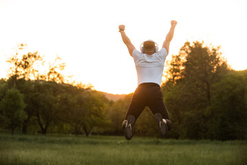 Fototapeta premium Success And Achievement Fit Man Jumping For Joy With Headphones Outdoors At Sunset Celebrating Freedom Wellbeing And Healthy Lifestyle In Nature Expressing Happiness.