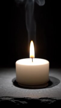 A lit candle with rising smoke is placed on a dark surface, viewed from a slight angle, capturing a serene ambiance in a photograph