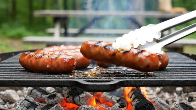 Sizzling sausages cooking on a charcoal grill outdoors at picnic