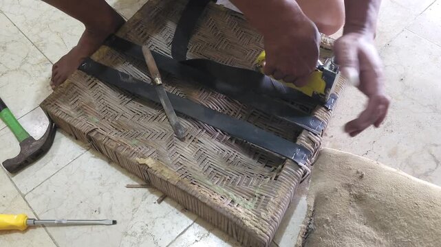 Close up of a handyman repairing a woven chair seat by stapling reinforcement straps to the wooden frame with tools on the floor